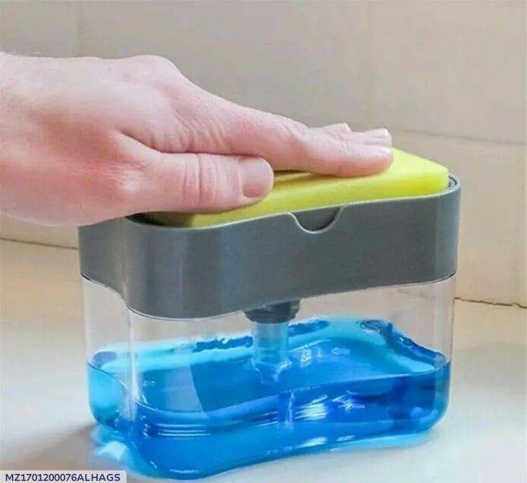 Modern plastic soap dispenser with gray top and transparent container filled with blue soap and integrated sponge holder being pressed by hand