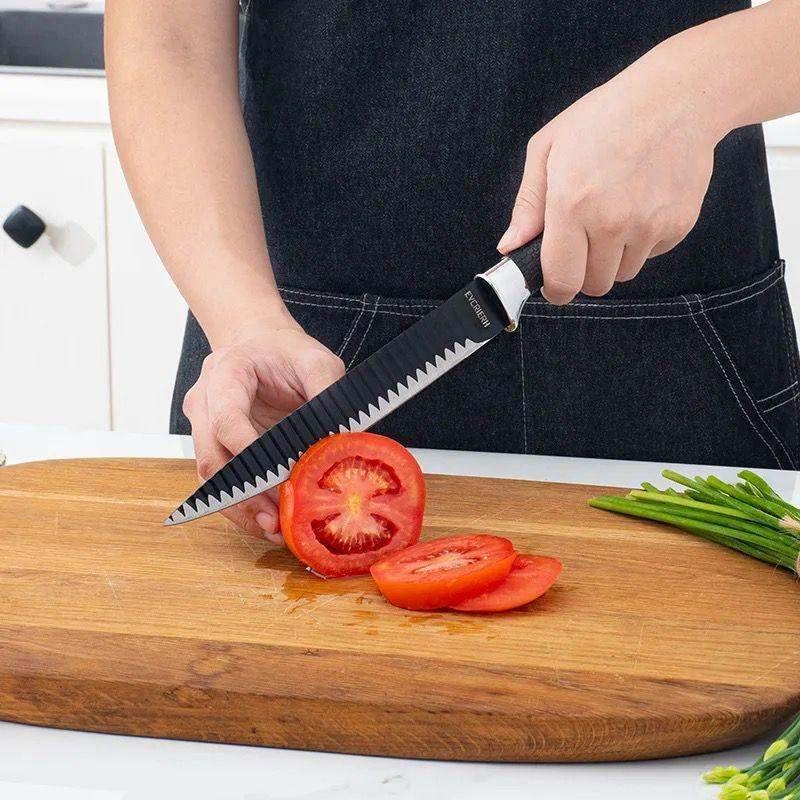 Wave pattern sharp stainless steel chef's knife slicing tomato on wooden cutting board