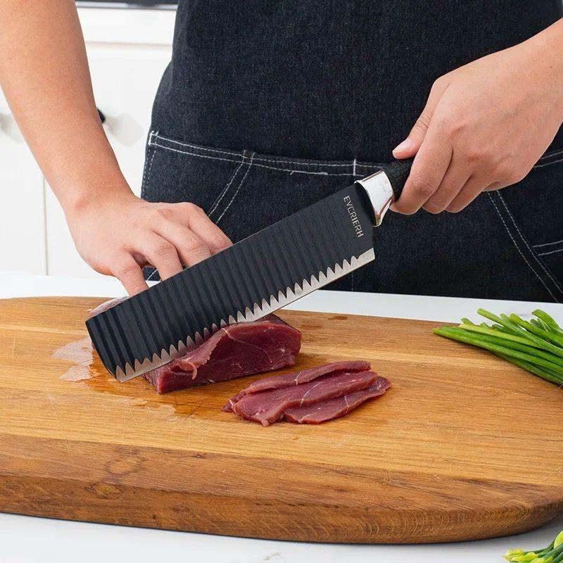 Wave pattern sharp chef's knife cutting meat on wooden cutting board in kitchen
